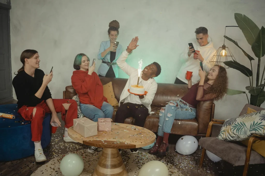 A group of young adults celebrate together with a giant cake that includes a big ol' flaming candle.