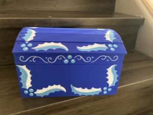 A blue treasure chest with icy blue and white boughs of holly painted around it.